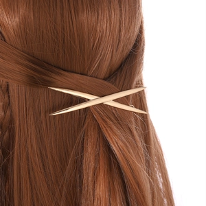Detail of a gold-finished geometric X-shape metal hair clip on brown hair
