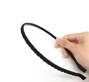 Dettaglio del cerchietto intrecciato nero tenuto in mano con trama in finto camoscio