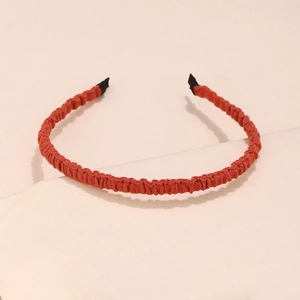 Minimalist pleated fabric headband in vibrant orange on a textured beige stone base