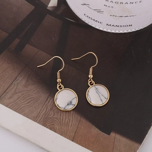Detalle de pendientes dorados minimalistas con textura de mármol blanco sobre una revista