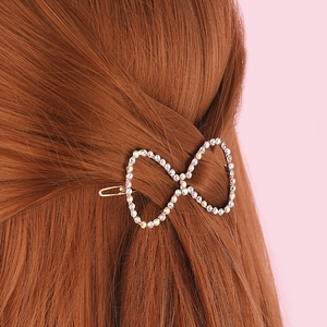 Golden bow hair clip with colorful rhinestones on auburn hair against pink background