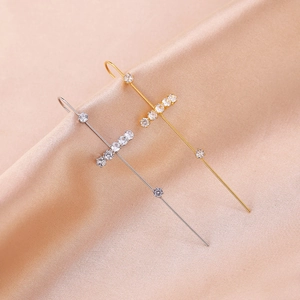 Macro shot of gold and silver cross ear crawlers with sparkling zircon on satin fabric