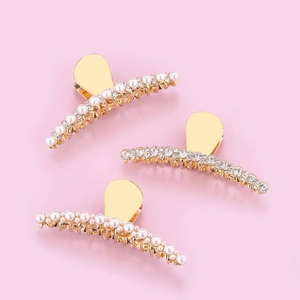 Drei elegante goldene Haarklammern mit Perlen und Strass auf weichem rosa Hintergrund
