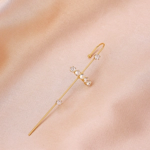Detail of a gold cross ear crawler with sparkling zircons on elegant champagne satin fabric