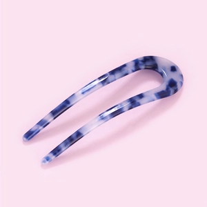 Detail view of blue and white marble acetate U-shaped hair pin on a pink background