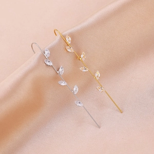Macro shot of gold and silver leaf ear crawlers with marquise-cut zircon stones on silk