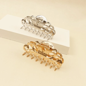 Elegant gold and silver metal hair claw clips with hollow design on beige texture backdrop