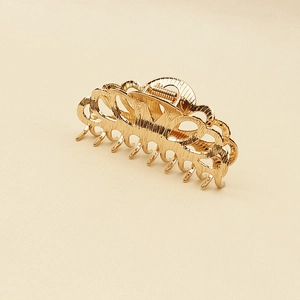 Detail view of large gold metal hair claw clip with hollow wave design and brushed finish