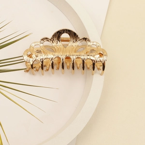 Detail of golden metal crown hair claw clip with elegant brushed texture on white tray