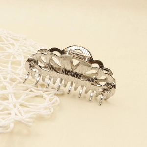 Close-up of silver metal hair claw clip with hollow wavy design and polished finish