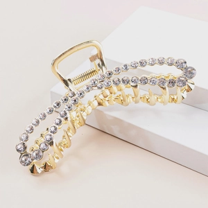 Close-up of golden metal hair claw clip with rhinestones on a white geometric stand