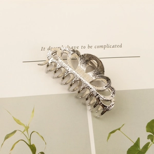 Close-up of a silver metal hair claw with hollow wave textures and polished finish
