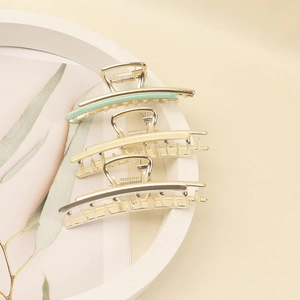 Three elegant gold metal hair claws with enamel details in green, cream, and silver grey