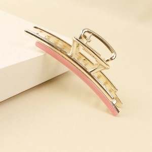 Detail view of a golden alloy hair claw clip with pink enamel inlay on stone surface