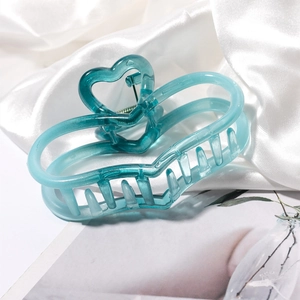 Detail of a cyan hollow heart hair claw clip on white satin fabric and a magazine