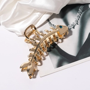 Detailed view of gold fishbone hair claw clip with a navy blue rhinestone on white silk
