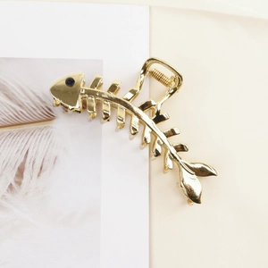 Close-up of golden fishbone hair claw clip featuring a blue rhinestone on a fabric surface