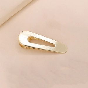 Detail of golden brushed metal hair clip with a hollow teardrop shape and matte finish