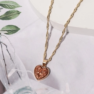 Nahaufnahme des Herzanhängers mit orange-rosa Kristallstruktur und goldener Kordelkette
