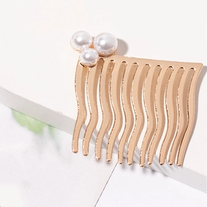 Détail du peigne en métal doré avec dents ondulées et trois perles blanches élégantes