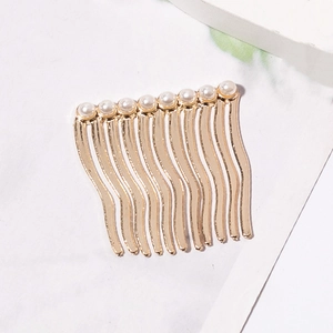 Détail d'un peigne à cheveux en métal doré avec dix dents et huit perles blanches