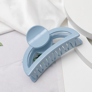 Détail d'une pince à cheveux bleu clair mat sur un fond de tissu blanc minimaliste