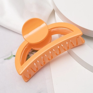 Gros plan d'une pince à cheveux orange brillante sur un socle blanc minimaliste