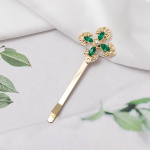 Detailed view of golden metal hair clip featuring green marquise crystals and a center pearl