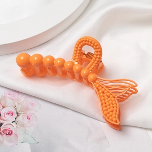 Détail d'une pince à cheveux orange en forme de queue de sirène sur tissu en soie blanche