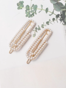 Close-up of pearl hair clips with gold metal base and white faux pearls on leaf background