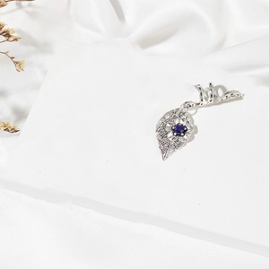 Detail of silver leaf braid ring with blue gemstone on white geometric pedestal
