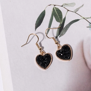 Fashionable gold heart drop earrings with black resin druzy stones on a floral background