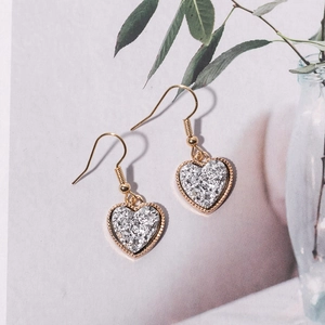 Close-up of golden heart-shaped drop earrings with shimmering silver crystal texture
