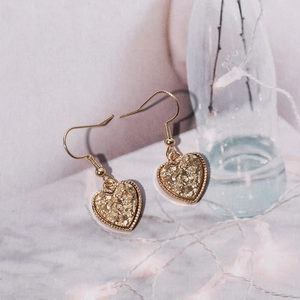 Detail shot of heart-shaped drop earrings with golden resin texture and metal hooks
