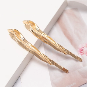 Elegant gold wavy fluid hairpins set displayed on a minimalist marble background