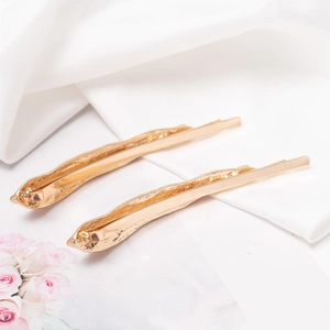Elegant gold metal hair clips with irregular texture on white silk background