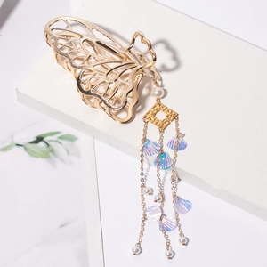 Détail d'une pince à cheveux papillon dorée avec glands en perles et breloques coquillage