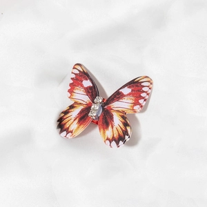 Detailed close-up of a realistic orange butterfly hair clip with sparkling rhinestones