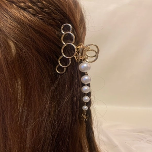 Détail de la pince à cheveux dorée avec pampille de perles sur cheveux bruns