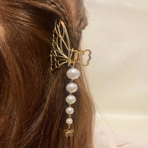 Détail d'une pince à cheveux papillon dorée avec pompon de perles blanches élégantes