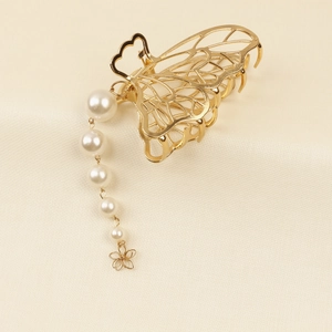 Détail de la pince à cheveux papillon dorée avec pompon en perles sur tissu doux
