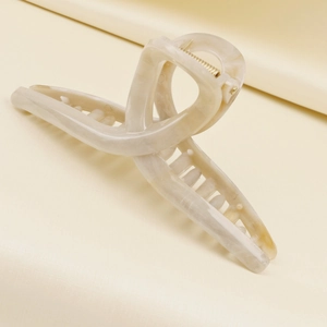 Detail of cream marble hair claw clip with golden metal spring on silk background