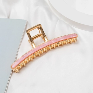Detail of golden metal claw clip with pink marble resin inlay on white silk fabric