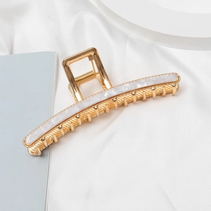 Detail of metal hair claw clip with white marble texture and gold alloy finish
