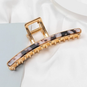 Detailed close-up of golden metal hair claw with marble texture resin inlay on silk