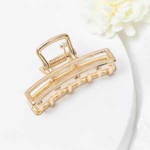 Macro detail of golden rectangular hollow hair claw clip with sturdy metal spring