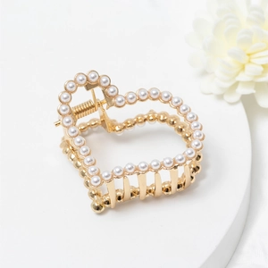 Elegante pinza per capelli a cuore dorata con perle bianche su un piatto bianco