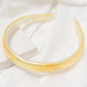 Détail d'un serre-tête transparent rempli de paillettes dorées sur satin blanc
