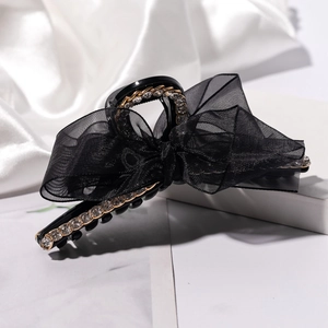 Détail de la pince à cheveux avec nœud en maille noire, chaîne dorée et strass