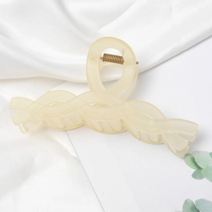 Close-up of beige matte resin hair claw clip with twisted texture and gold metal spring